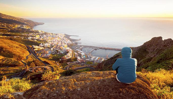 Young female traveler in blue jacket enjoying landscape view on Santa Cruz city on La Palma island in the morning