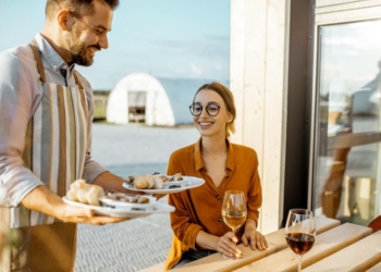 Waiter serving delicious dish with stuffed snails to a young woman client at the restaurant outdoors. Restaurant with own production of snails