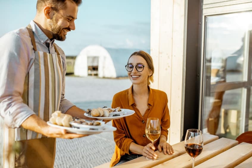 Waiter serving delicious dish with stuffed snails to a young woman client at the restaurant outdoors. Restaurant with own production of snails