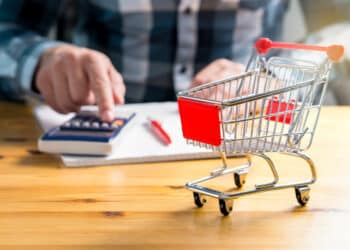 Rising food and grocery store prices and cost of living concept. Man counting food and consumer goods money with pen, paper and calculator at home. Budget of disadvantaged and low income family.