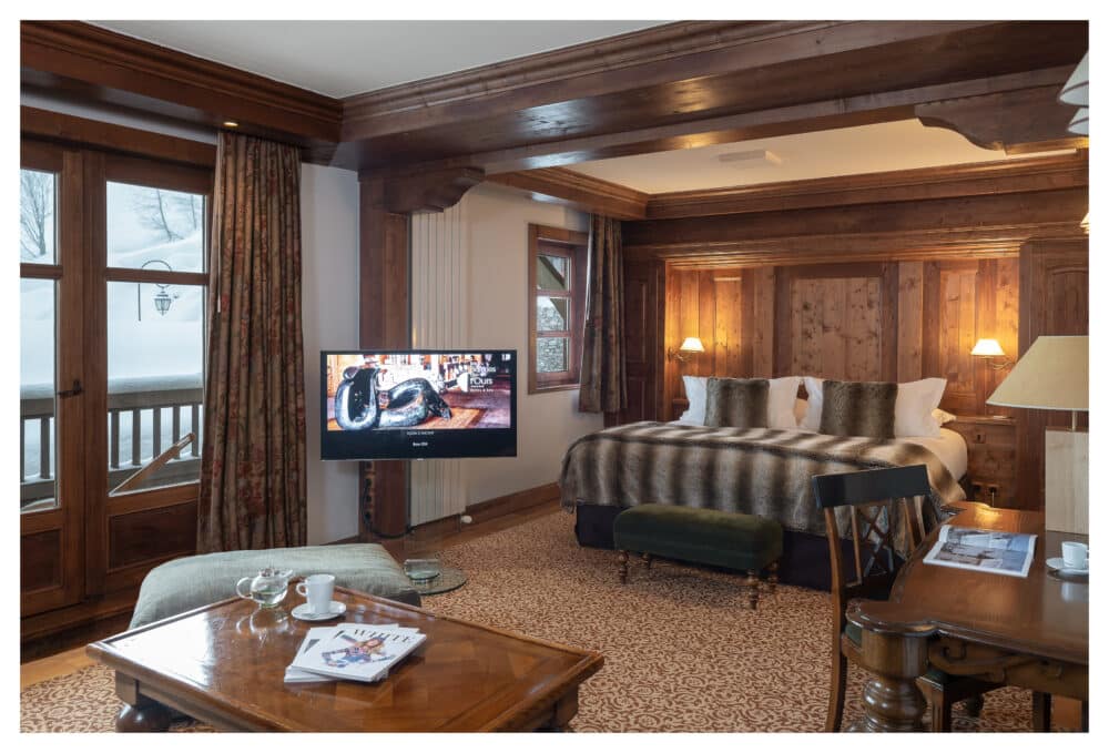 grande chambre marron avec coin salon, luminaire, télé allumée