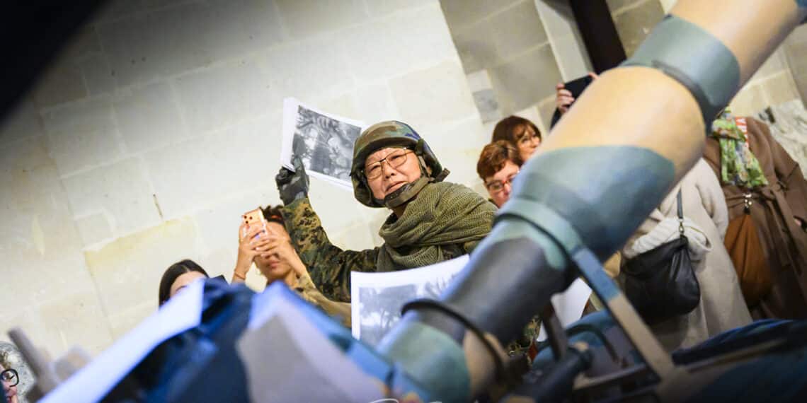 Homme habillé en soldat derrière un canon de char et qui lance un journal