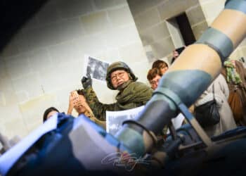 Homme habillé en soldat derrière un canon de char et qui lance un journal