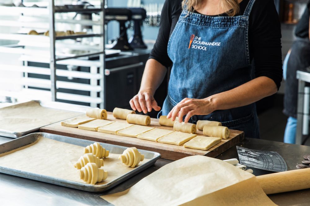 femme en tablier préparant des mini croissants en roulant la pâte