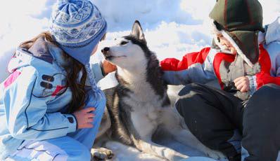 2 enfants accroupis dans la neige avec un chien de traîneau au milieu les regardant