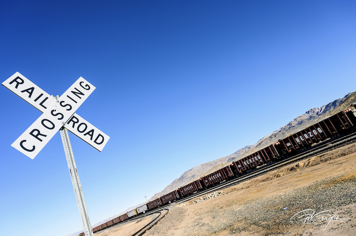 Un panneau en croix et derrièer un long train de wagon dans le désert sous un ciel bleu