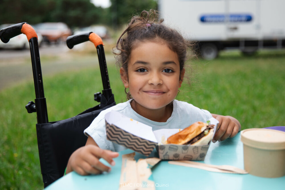 petite fille en fauteuil mangeant un burger avec un livre
